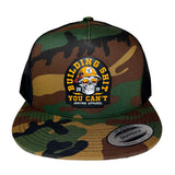 A camouflage trucker hat with a snapback closure, featuring a large embroidered patch on the front with a skull and the text 'BUILDING SHIT YOU CAN'T' and 'JRNYYN APPAREL'.
