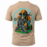 A tan t-shirt shown from the back, featuring a large graphic of a skeleton construction worker wearing a hard hat and holding a wrench, with stacks of money and a city skyline. The text 'BUILDING SHIT YOU CAN'T' is printed in light blue around the graphic.