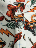Close-up of a white short-sleeve button-up shirt with a colorful retro tattoo-style print featuring orange hibiscus flowers, orange lightning bolts, green leaves, and a black-and-white skull wearing an orange hat. The inner neck label shows the brand JNHYMN.