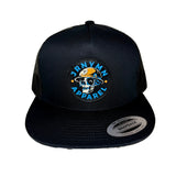 A black trucker hat with a circular embroidered patch on the front that reads 'JRNYMN APPAREL' around a skull wearing a yellow cap. A silver 'Snapback' sticker is visible on the brim, and the hat is photographed against a plain white background.