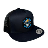 A trucker hat with a circular embroidered front patch featuring a skull in a yellow hard hat and the text 'JRNYMN APPAREL'. The cap has black mesh back panels