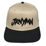 A structured snapback cap with a beige crown and a black flat brim, featuring the word 'JRNYYMN' embroidered in a black stylized font across the front.