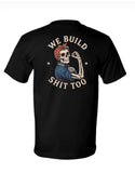 A black short-sleeve t-shirt shown from the back, featuring a large graphic print of a skeleton wearing a red bandana and blue shirt, flexing with a hammer. The text 'WE BUILD' is arched above the skeleton, and 'SHIT TOO' is written below in a distressed cream font.